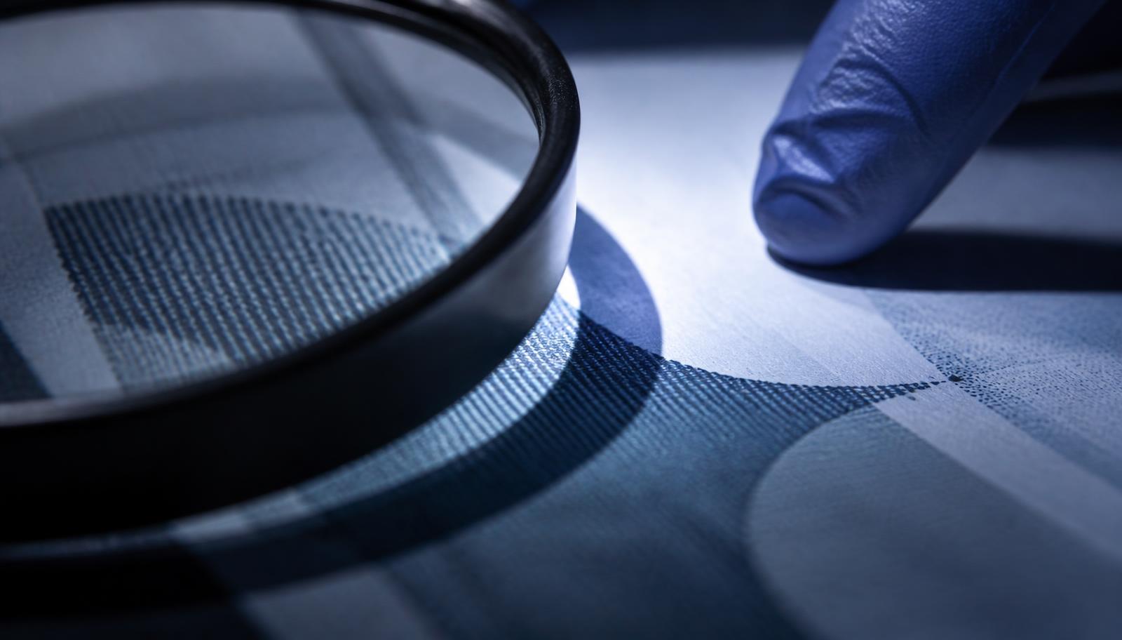 A document page examined under raking light with a magnifier and gloved fingertip in frame